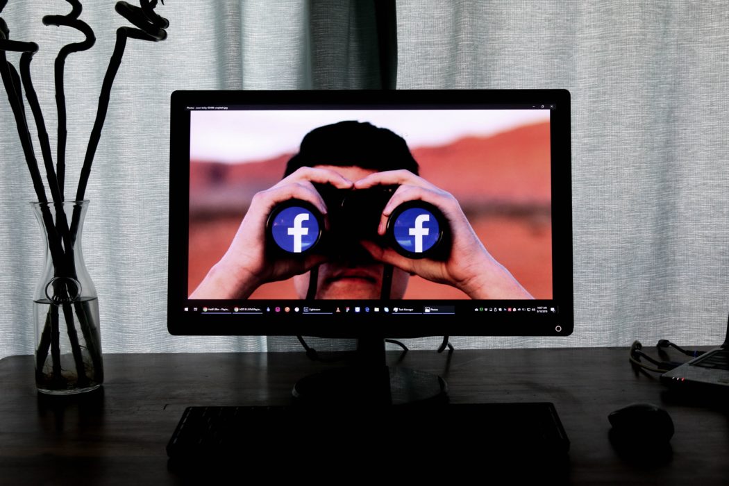 фото рабочий стол с компьютером, логотип фейсбука в бинокле