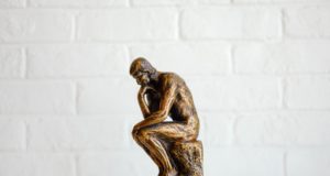 статуэтка мыслителя стоит на фоне белой кирпичной стены